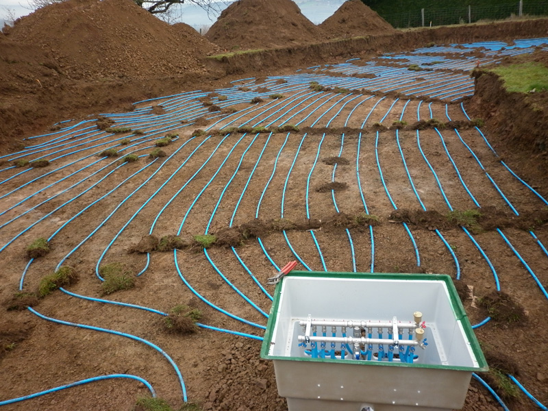 Installation de tuyaux de chauffage au sol en périmètre, avec gaine bleue sur chantier et coffret de contrôle en premier plan.