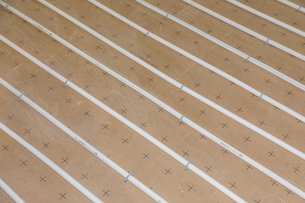Installation de tubes et rails de chauffage au sol sur isolation, avec pliage et fixations visibles.